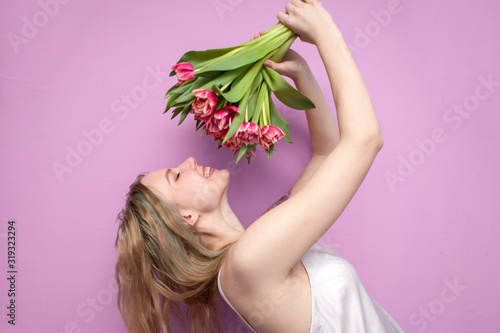 Fototapeta Naklejka Na Ścianę i Meble -  girl holds and sniffs a bouquet of flowers on a pink background, a beautiful woman with tulips