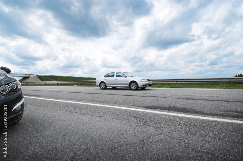 Fototapeta premium Cars on the countryside road against a cloudy sky