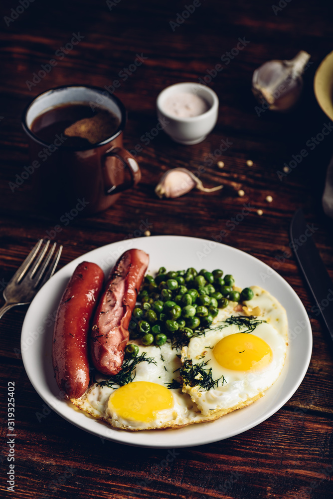 Breakfast with fried eggs, sausages and green peas on white plate