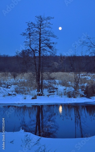 Scenery of early spring, night forest with a river that melts in ice and snow. Full moon and its reflection in the water.Awakening of nature.Enchanting night scenery outdoors photo