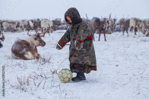 The Yamal Peninsula. Reindeer with a young reindeer herder. Happy boy on reindeer herder pasture playing with a ball in winter photo