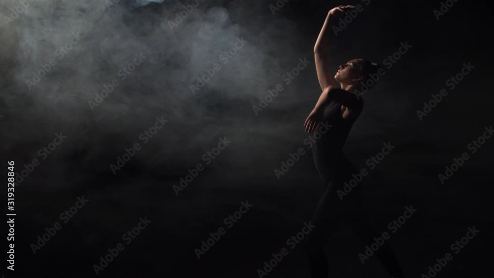 Faminine dancer in black outfit performing emotionally touching dance elements of contemporary choreography in twilight. Graceful young woman sansually dancing on gloomy stage in clouds of smoke Faminine dancer in black outfit performing emotionally touching dance elements of contemporary choreography in twilight. Graceful young woman sansually dancing on gloomy stage in clouds of smoke