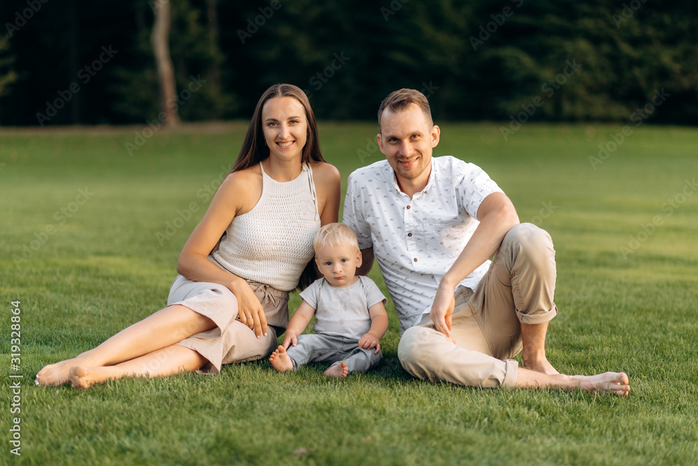 Family portrait of a happy family. Parents and their little baby boy are sitting on the grass and smiling