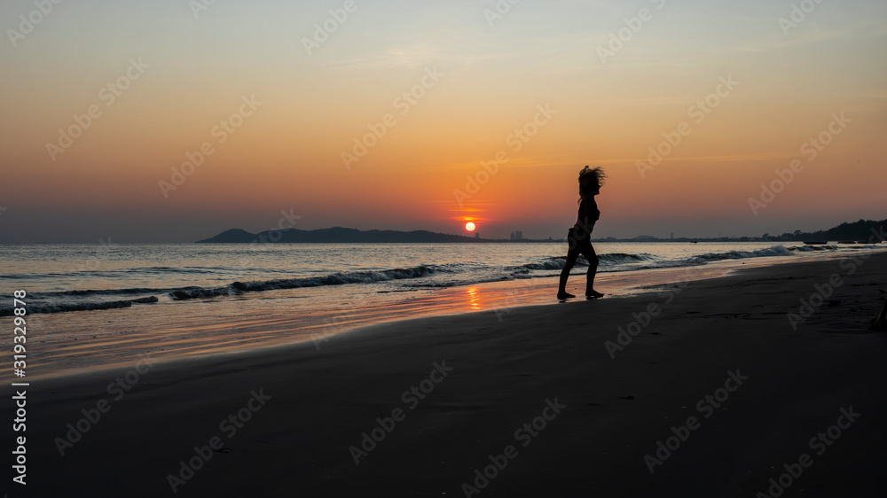 Silhouette of a child playing on the beach with a background of the golden glow of sunset and the reflections of the setting sun on the water.