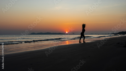Silhouette of a child playing on the beach with a background of the golden glow of sunset and the reflections of the setting sun on the water.