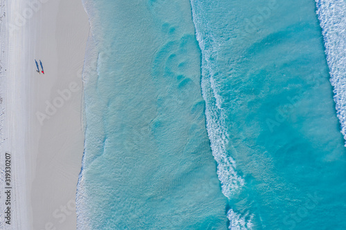 Overhead view of two people walking along Lucky Bay beach next to the clear turquoise water in Western Australia