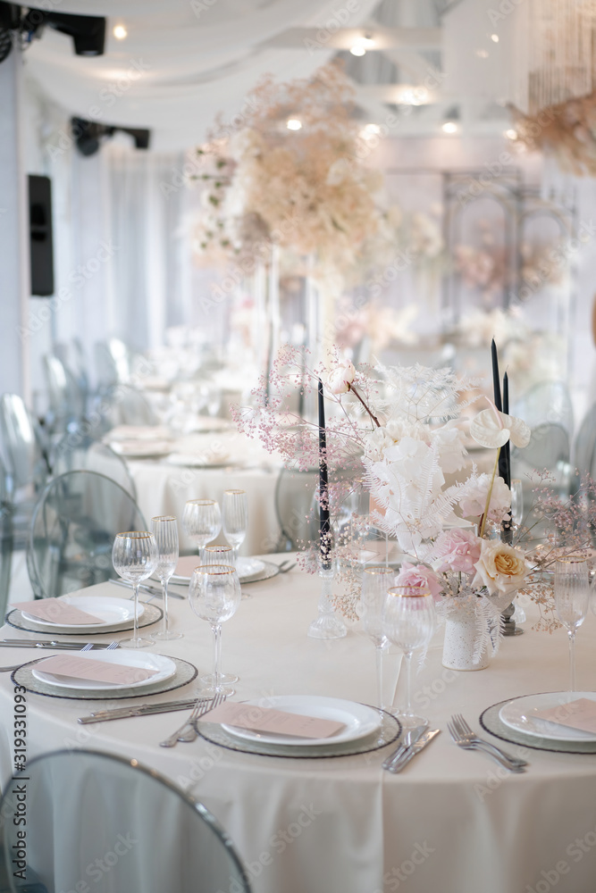 Decor of a wedding luxury dinner in white and pink colors. Served tables with silver and gold objects, plates, glasses and cutlery. Fresh flowers roses in vases.