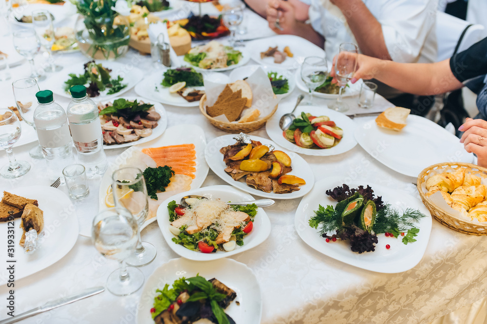 People are sitting at a table with a white tablecloth surrounded by plates of different foods. Lunch at the restaurant. People are sitting at a table with a white tablecloth surrounded by plates of different foods. Lunch at the restaurant.