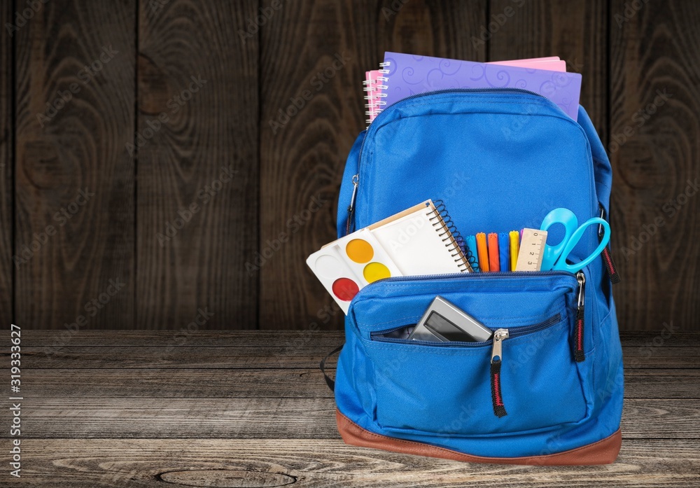 Naklejka premium Colorful school supplies in a backpack on wooden background