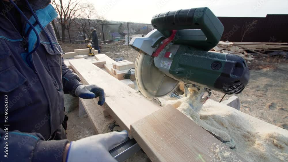 VLADIVOSTOK, RUSSIA - DECEMBER 1, 2019: Close view of circular saw cutting wooden plank and sewdust flying around. Frame house building VLADIVOSTOK, RUSSIA - DECEMBER 1, 2019: Close view of circular saw cutting wooden plank and sewdust flying around. Frame house building
