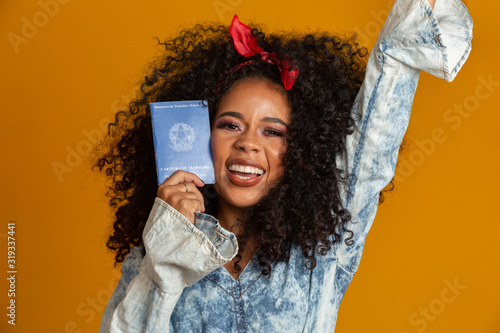 Beautiful curly-haired girl holding a work card. On yellow background. photo