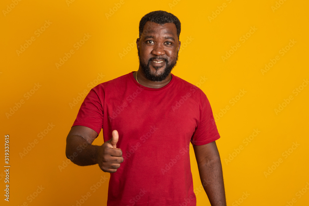 Positive dark skinned male has joyful expression and broad smile with white teeth, being in good mood, thumbs up, ok, okay isolated over yellow studio wall with copy space. Brazilian middle aged guy. Positive dark skinned male has joyful expression and broad smile with white teeth, being in good mood, thumbs up, ok, okay isolated over yellow studio wall with copy space. Brazilian middle aged guy.