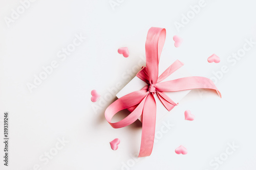 White gift box with pink ribbon and a small pink hearts on white background. Top view. Copy space