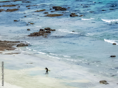 Wonderful sea view with an unrecognizable surfer walking alone on seashore holding his surfboard - Perfect clean shot from the top 