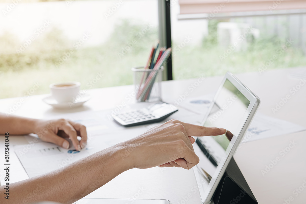 Obraz premium Business woman hand pointing at screen of laptop computer, analysing about business data project with calculator and a cup of coffee on the wooden table at office.