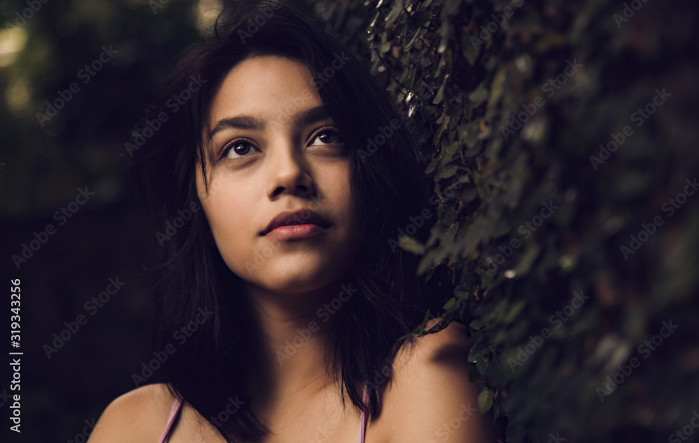 Beautiful and attractive young woman with contemplative look leaning against a wall with natural grass, young woman thinking about life Beautiful and attractive young woman with contemplative look leaning against a wall with natural grass, young woman thinking about life