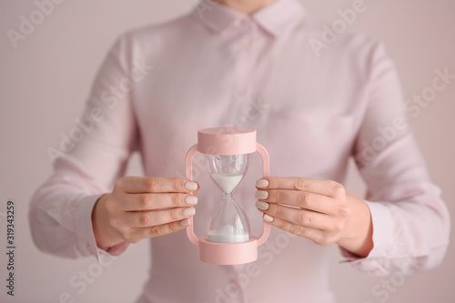 Woman with hourglass on light background, closeup. Time management concept photo