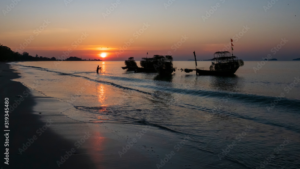 Fototapeta premium Silhouette of a traditional Thai fishing boat with a background of the golden glow of sunrise and the reflections of the rising sun on the water.