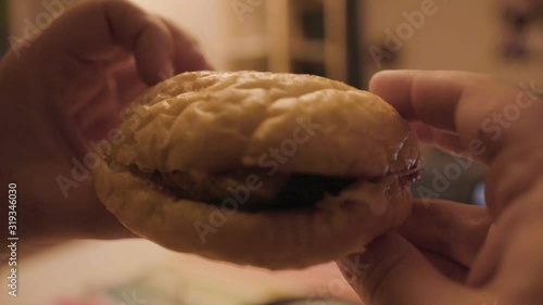 Man holding homemade hamburger. Stock footage. Close-up of hands holding small ugly hamburger cooked at home in hurry. Homemade gamberger on background of room photo