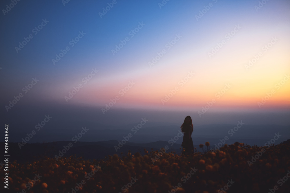 Silhouette image of a woman standing among beautiful flower garden on the top of the hill before sunrise