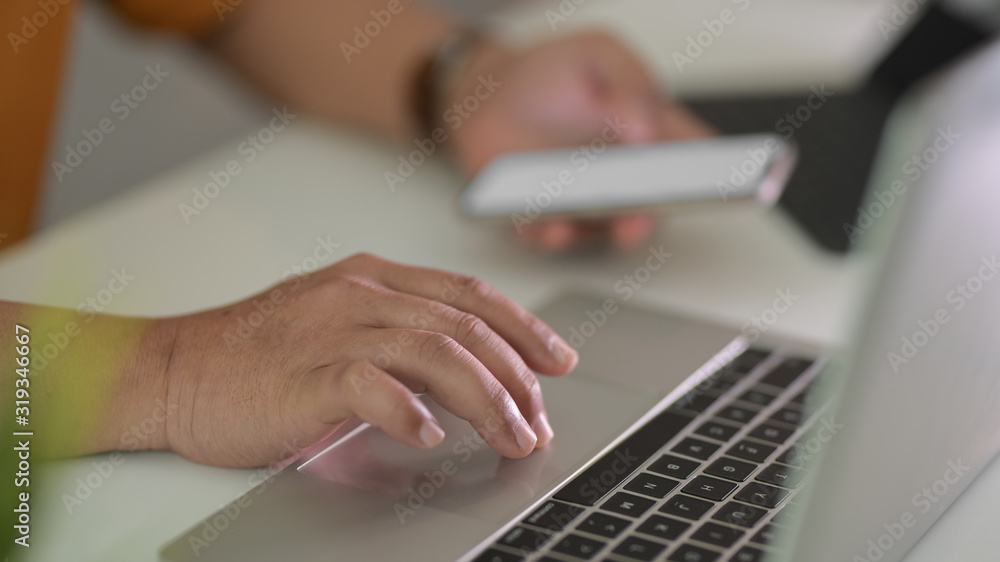 Side view of male freelancer typing on laptop while holding smartphone in workspace Side view of male freelancer typing on laptop while holding smartphone in workspace