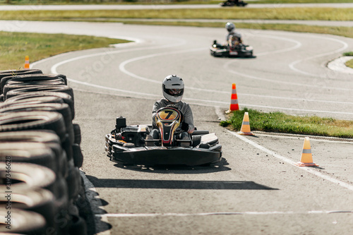 a man in a gray sweatshirt and jeans, in a white helmet drives a black kart with number 7 on an asphalt track