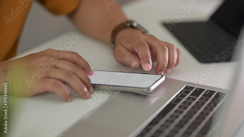 Side view of male freelancer typing on smartphone in workspace with laptop and office supplies © bongkarn