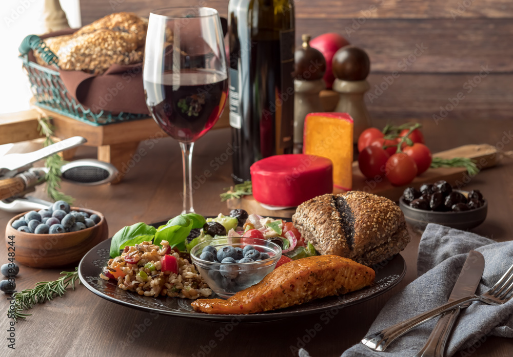 Close up view of a Mediterranean meal with foods including salmon, seven grain and greek salad. Served with red wine.
