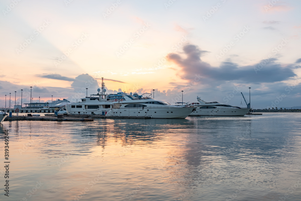 Beautiful orange sunset in the sea harbor with moored yachts. Expensive 92 foot yacht at the pier during sunset