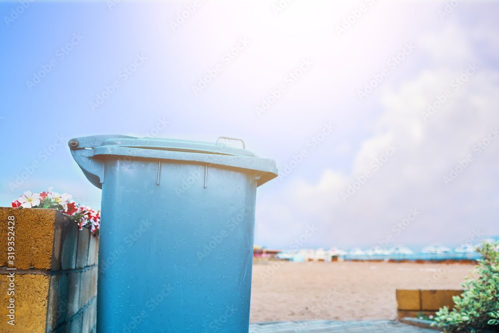 Naklejka premium Trashcan on the beach. Blue waste bucket on the shore of the lake.