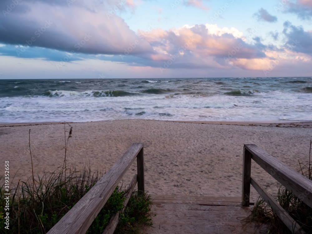 Wooden Pier Leading to the Sandy Beach and Ocean in Florida with a colorful cloudy sky before sunset.