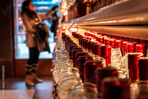 Perspective view of a bokeh of a woman shopping for wine or other alcohol in a liquor store standing in front of shelves full of bottles.