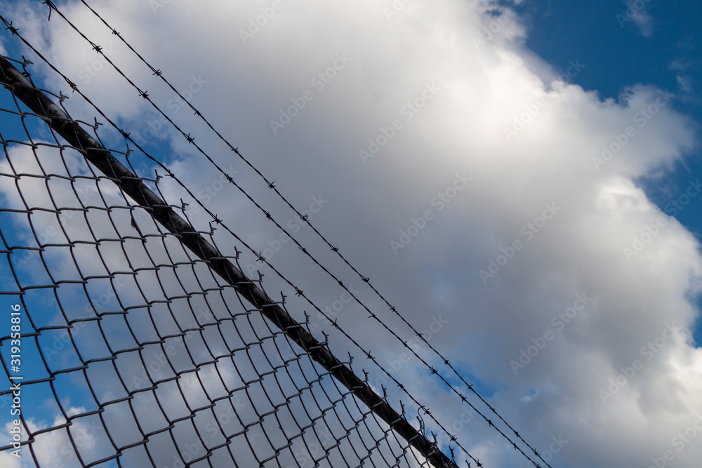 barbed wire silhouette fence with blue sky and white clouds barbed wire silhouette fence with blue sky and white clouds