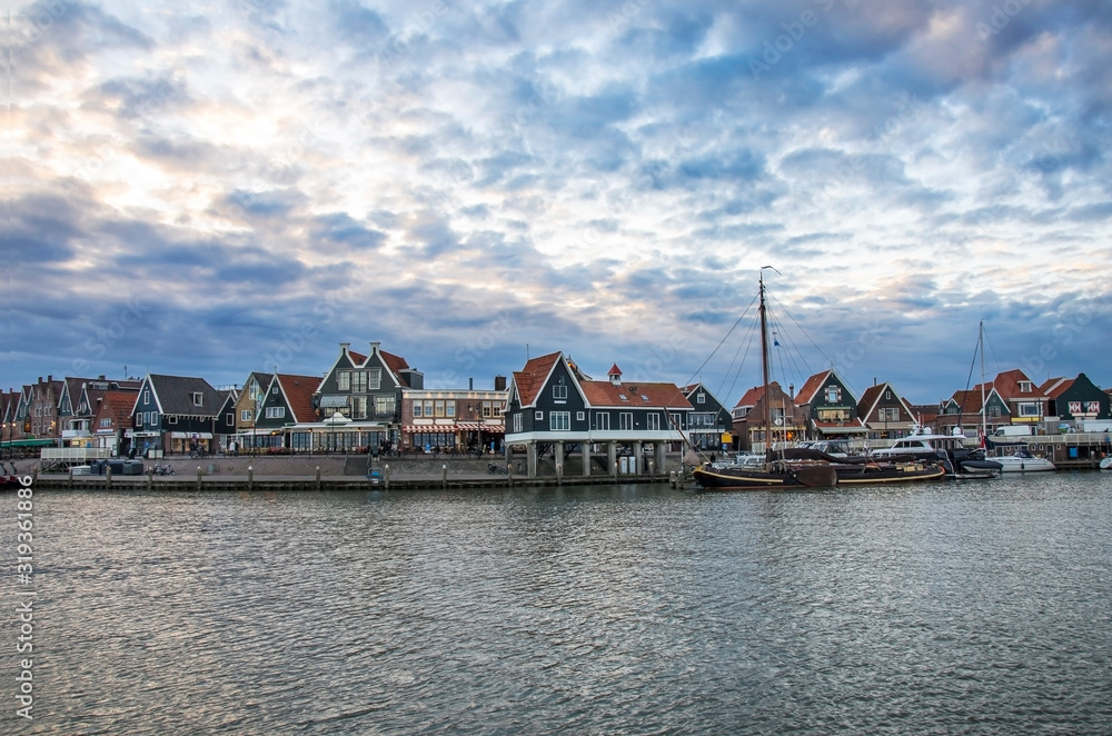 Fishing boats and yachts moored in marina in front of the traditional dutch wooden fishing houses in Volendam, Netherlands. Blue sky with heavy clouds. Fishing boats and yachts moored in marina in front of the traditional dutch wooden fishing houses in Volendam, Netherlands. Blue sky with heavy clouds.