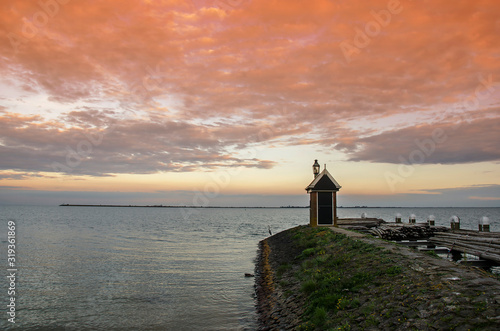 Sunset over pier, Volendam, Netherlands. Beautiful sunrise in pink tones over water and silhouette of small hut. Twilight over lake. © Maria Vonotna