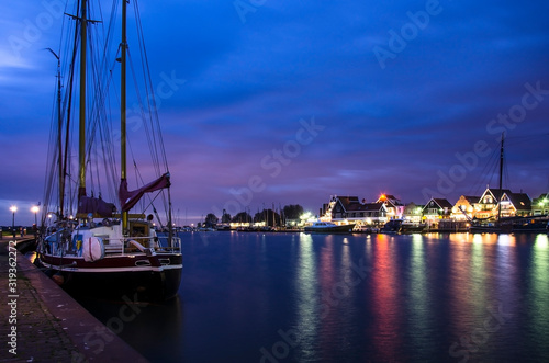 View of the Volendam harbor and yacht, boats and sailing boats anchored, Volendam, Netherlands. Marine with illuminated houses and blue sky.