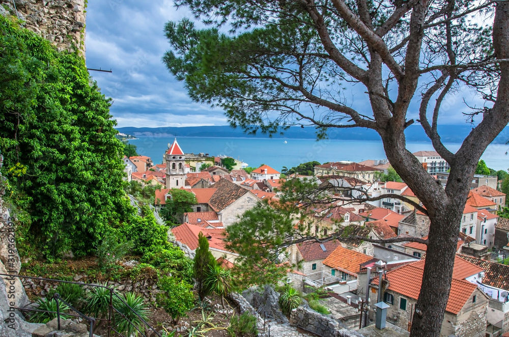 Aerial panoramic view of the small town Omis surrounded with mountains, Cetina river and sea, Makarska Riviera, Croatia. View of pine tree, old city center with red rooftops and blue see. Aerial panoramic view of the small town Omis surrounded with mountains, Cetina river and sea, Makarska Riviera, Croatia. View of pine tree, old city center with red rooftops and blue see.