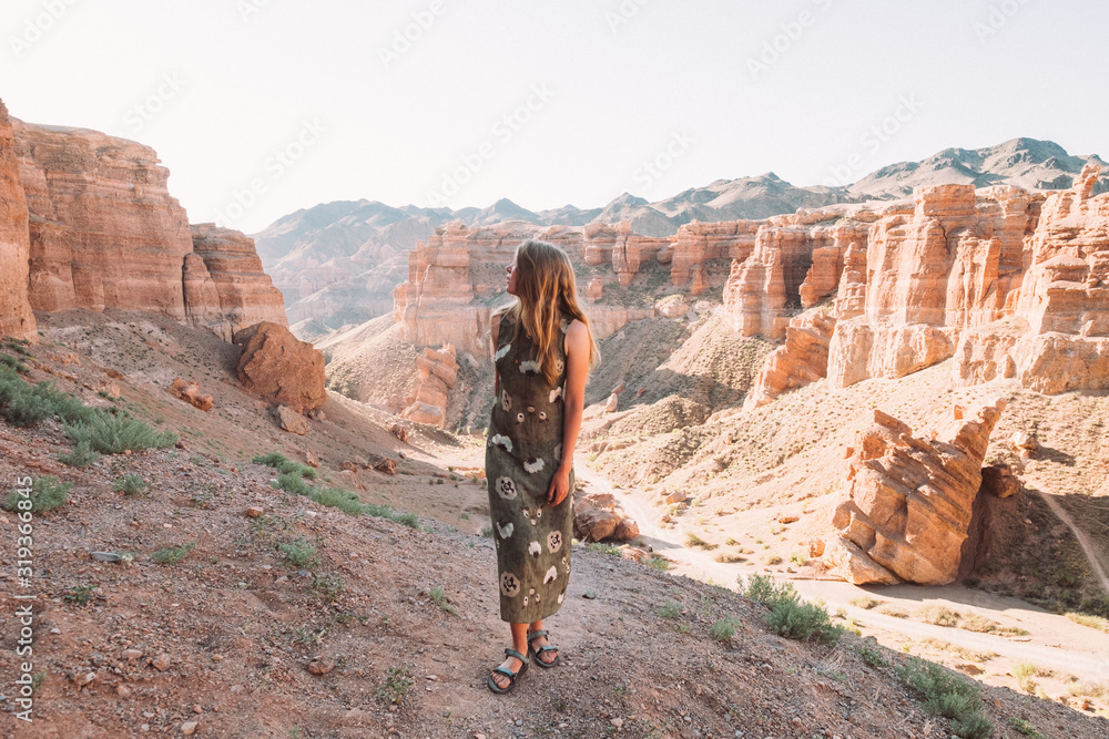 Charyn Canyon, Kazakhstan. Red-yellow canyon in yellow light. Looks like a famous grand canyon in America. Girl with her hair and a long light green dress on a background of nature. 