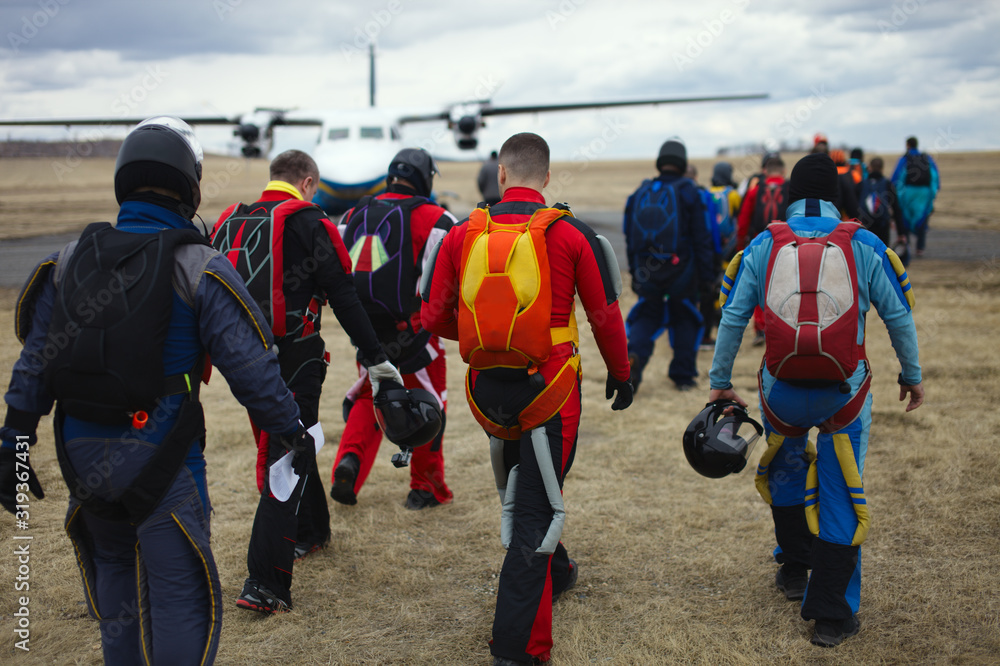 Obraz premium Team of skydivers with parachutes is walking to the plane before take-off, rear view, close-up.