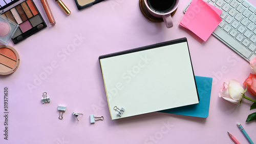 Top view image of feminine working desk including coffee cup, modern keyboard, notebook, pencil, bouquet and cosmetics putting on it. Women's working desk concept.