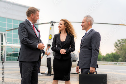 Three Businesswoman And Businessman In Discussion with Briefcase standing near helicopter when he arrive destination at helipad in airport with helicopter and captain standing near in background. photo