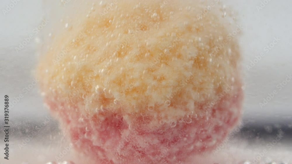 Underwater close up view of colorful bath bomb exploding and forming small bubbles in clean