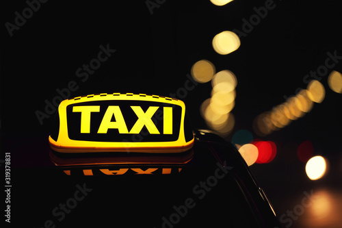Taxi car with yellow roof sign on city street at night, closeup