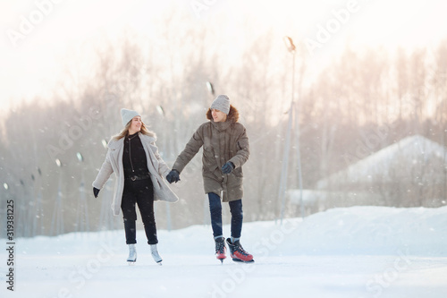 Happy young love couple hold hands, skate on rink, it snows in winter. Concept vacations outdoor activities