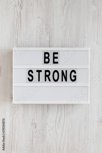 'Be strong' words on a lightbox on a white wooden surface, top view. Overhead, from above, flat lay.
