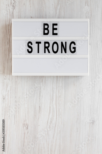 'Be strong' words on a lightbox on a white wooden surface, top view. Overhead, from above, flat lay. Space for text.