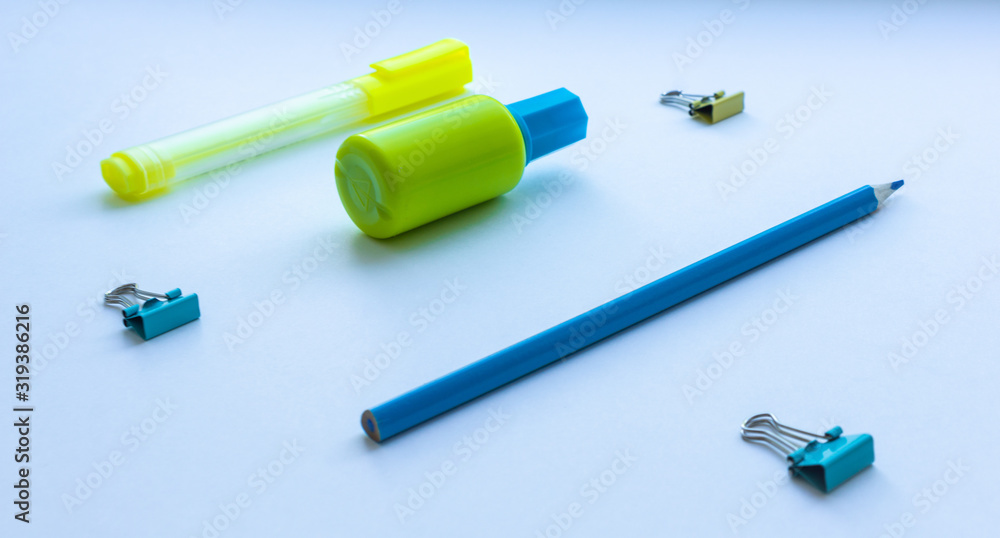 Mixed stationery in yellow and blue colours: clips, correction fluid, pencil and marker pen on white background. Concept of education, business, minimalism. Selective focus. Mixed stationery in yellow and blue colours: clips, correction fluid, pencil and marker pen on white background. Concept of education, business, minimalism. Selective focus.