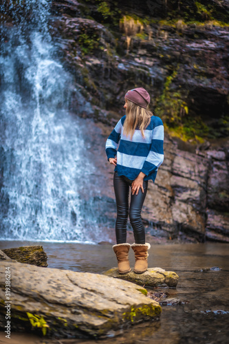 A straight-haired blonde with a blue and white wool sweater looking left at a waterfall. Lifestyle session