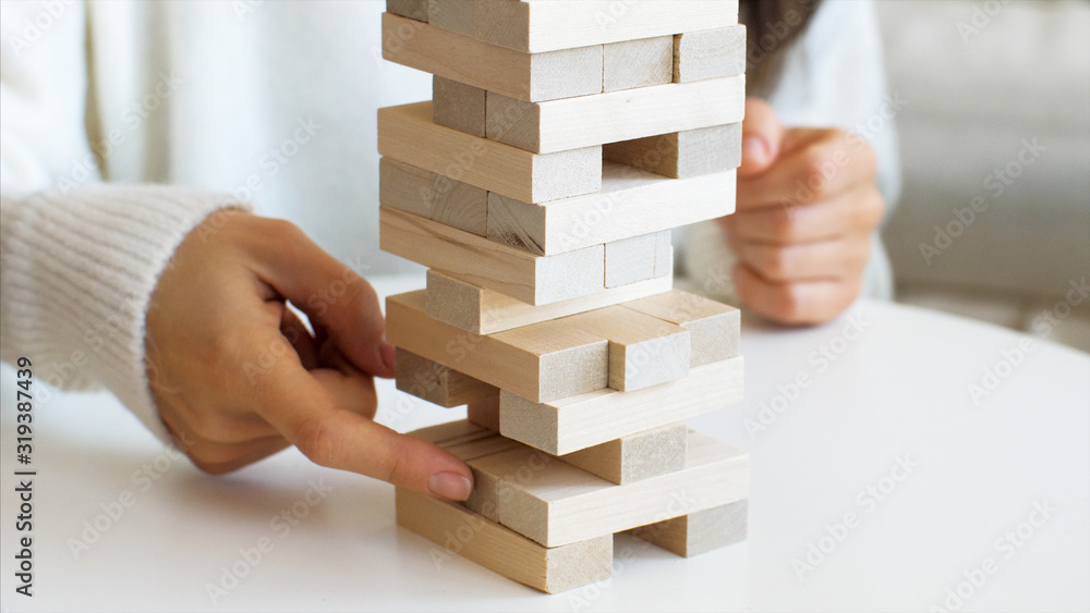Close-up of young woman's hands is pulling out the brick from wooden tower Close-up of young woman's hands is pulling out the brick from wooden tower