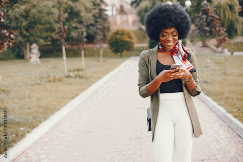 Fashionable girl in a summer city. Black lady in a green jacket. Woman in a red scarf. Famale with mobile phone